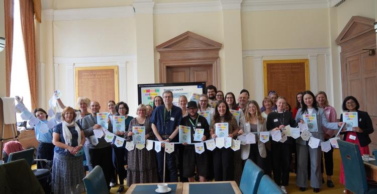 A photo of a large group of people together, they are holding what appear to be reports and a line of hand decorated bunting.