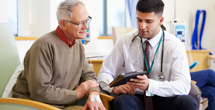 A photo of an older man talking to a doctor, the doctor is using a digital tablet to share information with the patient.