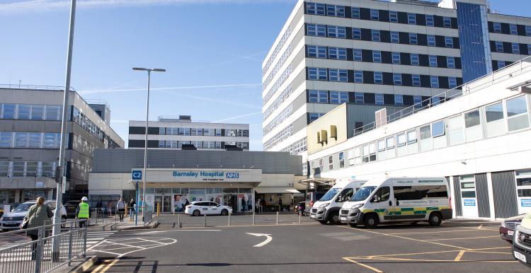 A photo of a hospital entrance at some distance, showing the car park and drop off