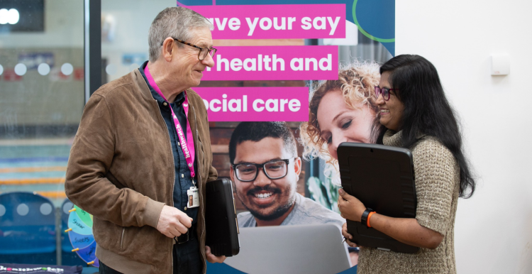 A photo of two people stood in front of a Healthwatch branded banner that reads 'Have your say on health and social care'