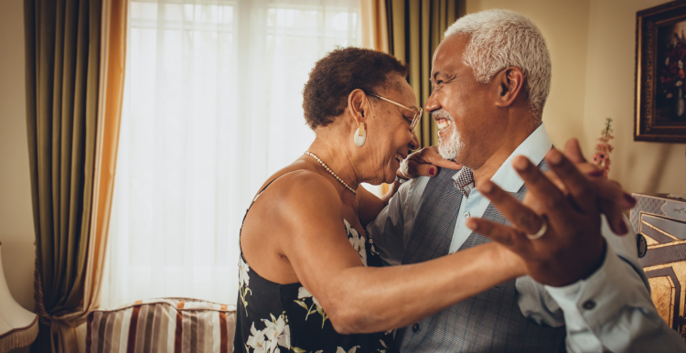 A photo of an older couple dancing together happily in a living room.
