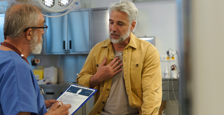 A photo of a man in a medical examination room talking to a doctor who is holding a clipboard