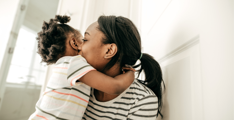 A photo of a woman with a young child. The child is hugging her and the woman's face is turned away from us.