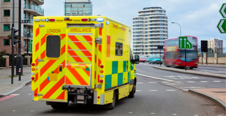 A photo of a London ambulance on the road, a red double decker can be seen in the background