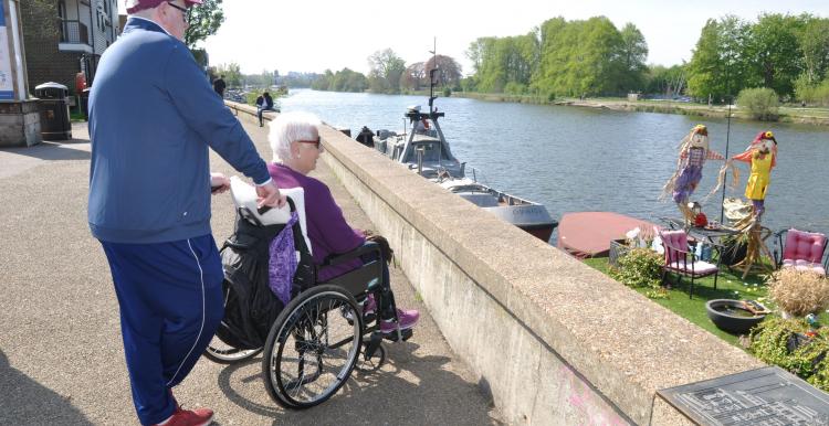 Man walking with lady in the wheelchair by the river 