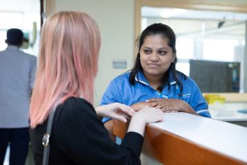 A photo of a woman at reception desk speaking to a worker in medical scrubs