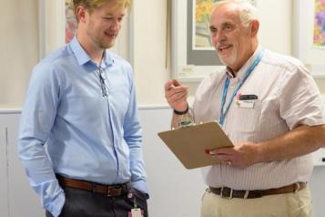 A photo of two people talking to each other, one is holding a clipboard and pointing