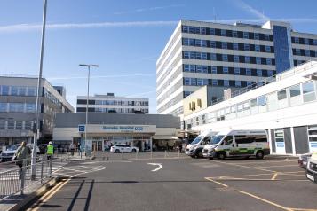 A photo of a hospital entrance at some distance, showing the car park and drop off