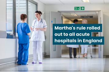 A photo of a hospital corridor with two medical staff speaking to each other. Text reads 'Martha's rule rolled out to all acut hospitals in England'