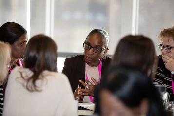 A photo of a group of people having a discussion. They are wearing formal clothes and matching bright pink lanyards.