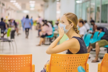 A photo of a woman in a busy hospital waiting room, she is wearing a face mask.