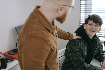 A photo of a supportive adult putting their hand on the shoulder of a younger person who is looking up at them and smiling.