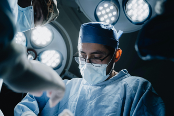 A photo taken at a low angle of a surgeon wearing a face mask while he operates.