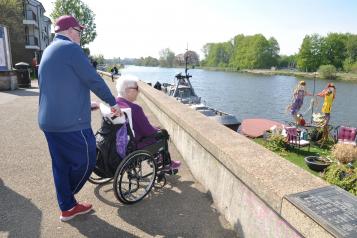 Man walking with lady in the wheelchair by the river 