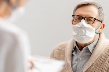 An elderly man wearing a face covering looking at a care worker