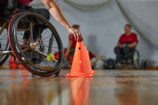 A photo of a man in a wheelchair in a sports hall placing a brightly coloured cone in preperation of an activity. 