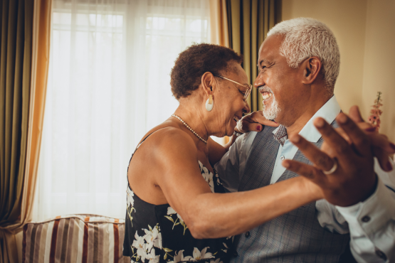 A photo of an older couple dancing together happily in a living room.