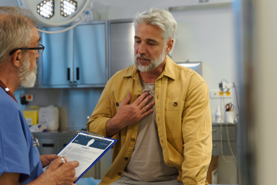 A photo of a man in a medical examination room talking to a doctor who is holding a clipboard