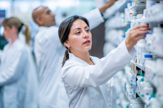 A photo of a woman in a pharmacy taking medicine from a shelf