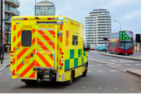 A photo of a London ambulance on the road, a red double decker can be seen in the background