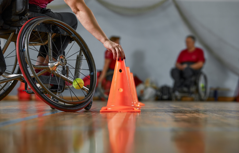 A photo of a man in a wheelchair in a sports hall placing a brightly coloured cone in preperation of an activity.