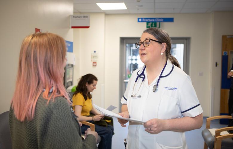 A photo of a woman talking to a medical professional in a hospital waiting room
