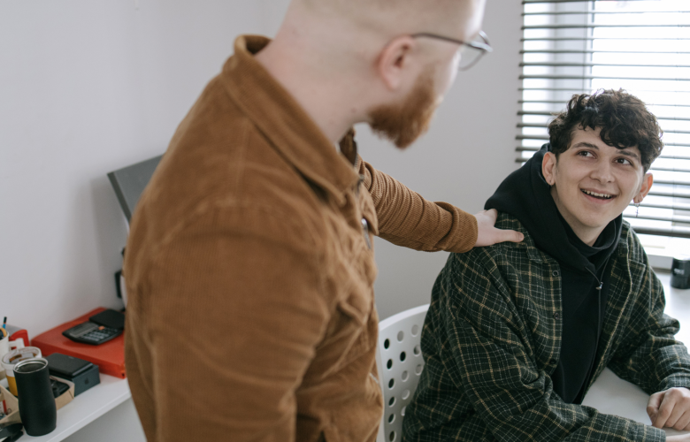 A photo of a supportive adult putting their hand on the shoulder of a younger person who is looking up at them and smiling.