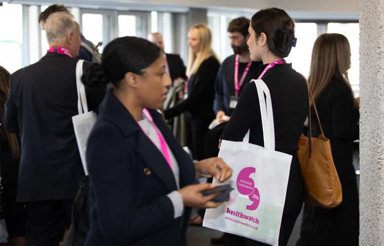 A photo of a group of people smartly dressed appearing to network. They are wearing white tote bags with bright pink healthwatch branding.
