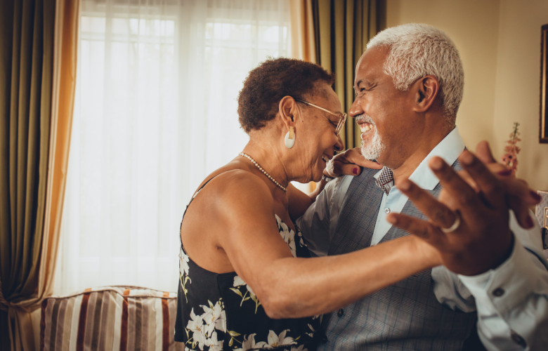 A photo of an older couple dancing together happily in a living room.