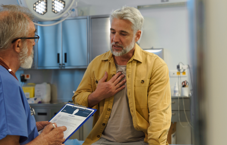 A photo of a man in a medical examination room talking to a doctor who is holding a clipboard