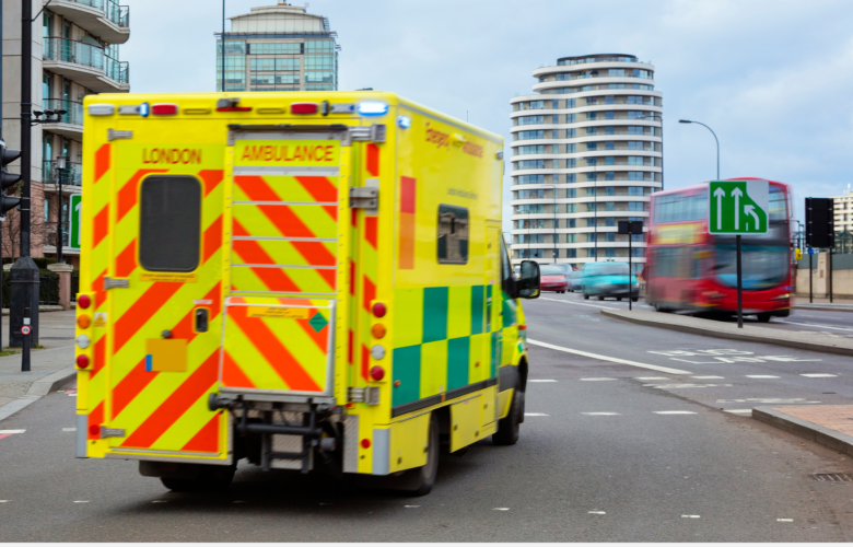A photo of a London ambulance on the road, a red double decker can be seen in the background
